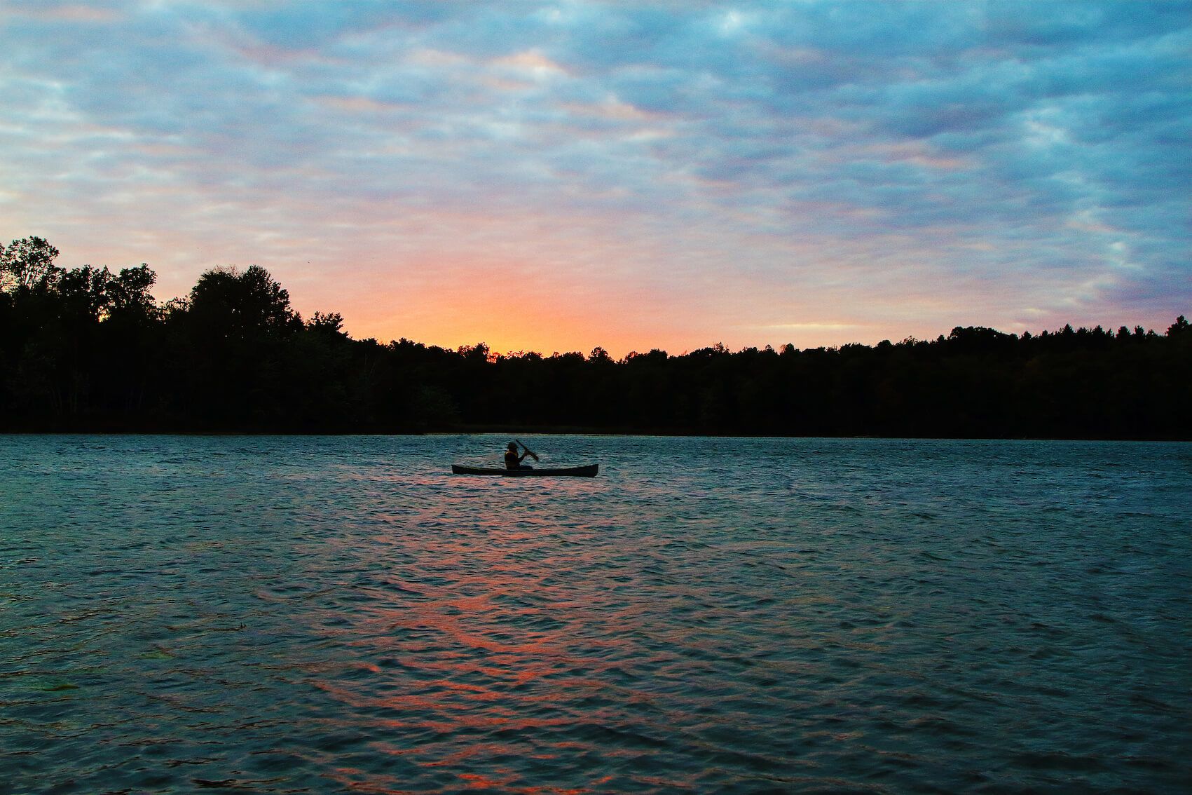 Person canoeing on serene lake at sunset