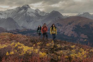 Three friends hiking in shoulder season to Nonda Peak between Toad River and Muncho Lake in the Northern Rockies, with views of the Sentinel mountain range in the background.