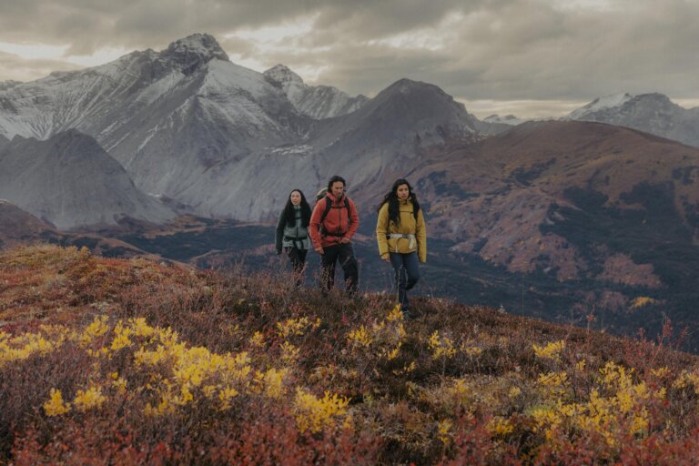 Three friends hiking in shoulder season to Nonda Peak between Toad River and Muncho Lake in the Northern Rockies, with views of the Sentinel mountain range in the background.
